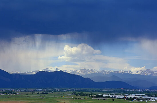 looking out at prairie and  the virga clouds of an afternoon thunderstorm in  the snow-capped peaks of the front range of the colorado rocky mountains, as seen from broomfield, colorado 