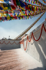 Boudhanath Stupa wall decorated with garlands of velvets (mala) and prayer flags above it. Kathmandu, Nepal