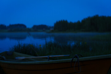 A still lake at midsummer night with a close up of a rowboat on shore.