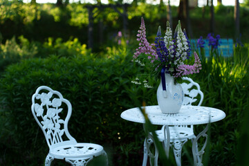 White garden furniture with flowers on the table in a green garden setting.