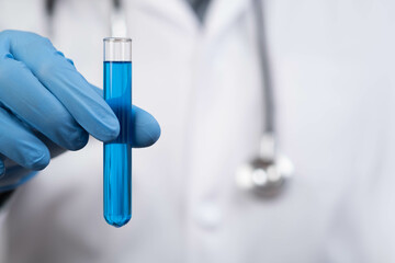 A person in medical attire holds a test tube containing blue liquid, highlighting laboratory work...