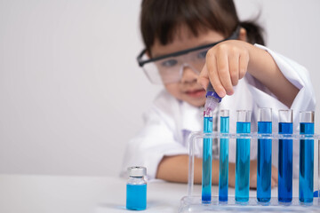 A young child in protective glasses conducts an experiment with colorful liquids in test tubes,...