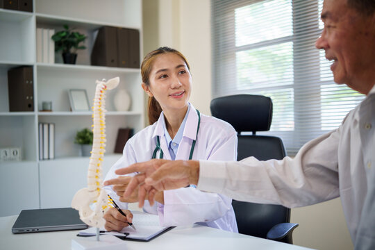 Orthopedic doctor educating aging patient about spinal health and posture using a human spine model. - Powered by Adobe