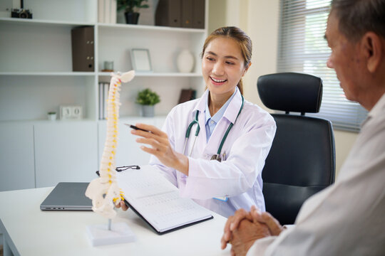 Orthopedic doctor educating aging patient about spinal health and posture using a human spine model.