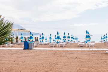 Empty beach with rows of closed umbrellas and sun loungers on a cloudy day. Coastal relaxation, off-season atmosphere and summer tourism infrastructure.