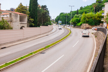 City street with cars and Mediterranean greenery in Montenegro. Urban infrastructure and road transportation in a coastal town.