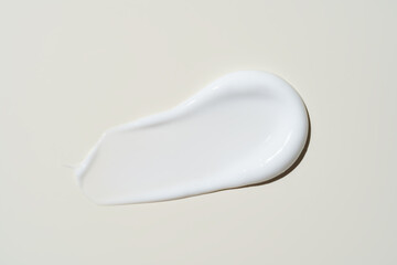 Close-up of a finger swiping rich face cream across a beige backdrop, capturing its velvety texture...