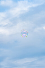 A shimmering soap bubble floats against a bright blue sky, reflecting iridescent rainbow colors....