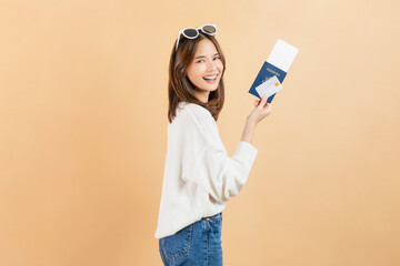 Happy smiling young Asian woman holding passport with plane tickets and credit card in beige color background. Tourist travel trip journey concept.