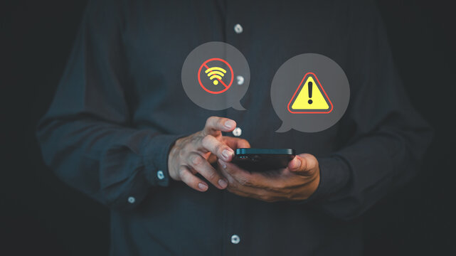 Person holding a smartphone with no Wi-Fi and warning alert icons, representing connection failure, network error, or internet outage issue. - Powered by Adobe