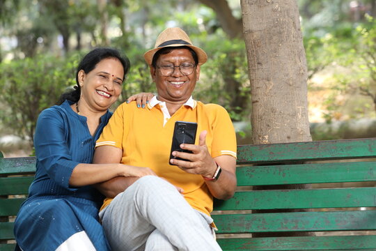 Indian senior happy couple using mobile phone at the park.