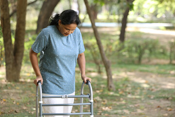 Unhealth Indian senior woman walking with walker in park. Concept of adult health insurance