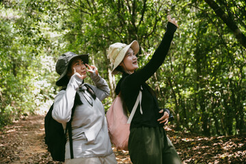 Two female friends with backpacks on vacation hiking through countryside together. Asian friend...