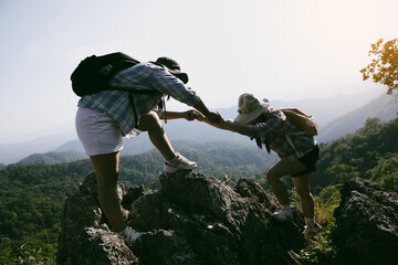Two friends helping with teamwork trying to reach top of mountains during wonderful summer sunset....