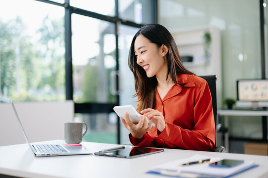 Smiling Asian woman using laptop, tablet, and digital pen at office desk. Concept of remote work, freelance, creativity