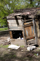 Close-up of abandoned wooden shack with broken door and scattered debris on the ground