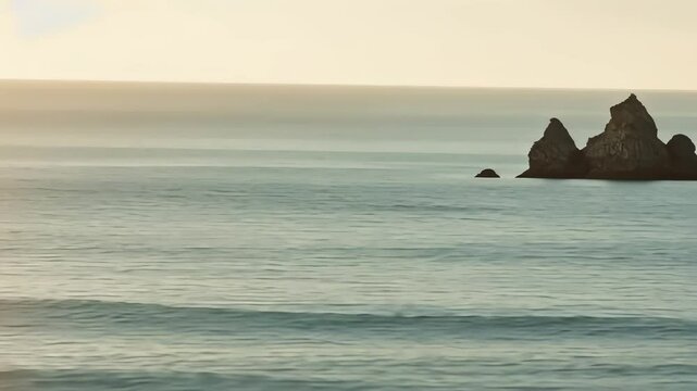 Panoramic view of ocean with large rock formations and a distant ship at sunset, serene landscape footage.