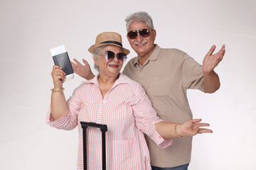 Portrait of indian Senior couple tourists studio standing isolated on grey background studio holding passports wearing stylist sunglasses and plane tickets looking camera smiling cheerful lifestyle.