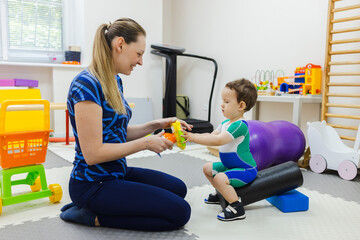 Female physical therapist training a young child in physical skills of standing up and sitting down...