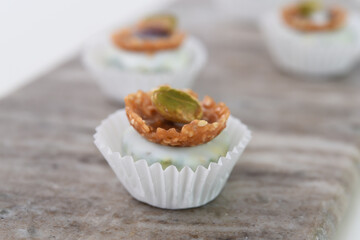 Mini Dessert in a white paper cup possibly white chocolate or cream, topped with a unique crunchy sesame seed crisp side view of sweet bite