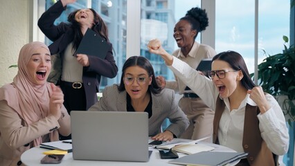 Excited shocked multiethnic women females businesswomen team colleagues multiracial group looking laptop computer celebrating win shock business offer deal success applause indoor office meeting room