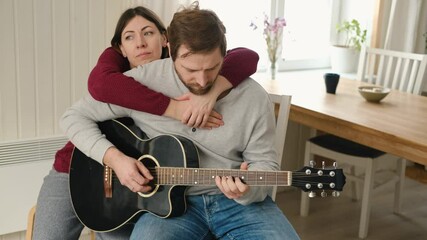 Happy couple in love dating. Man plays guitar to his girlfriend. Husband playing acoustic guitar for his wife at home. Anniversary. Enjoying music together. intimate moment. Playing guitar together - Powered by Adobe