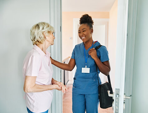 Doctor or nurse caregiver with senior woman at home or nursing home, a caregiver standing on the front door arriving and being welcomed by a senior woman - Powered by Adobe