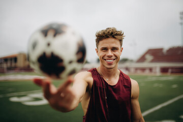Smiling male soccer player spinning ball on finger at football field
