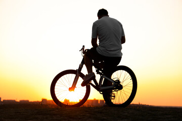 Cyclist resting on horizon line of road against the backdrop of hills at sunset. Black silhouette...