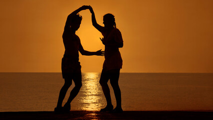 latin  couple is dancing bachata above sea on summer sea beach Sunset over water. Two silhouettes...