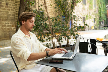 Young man working quietly on laptop in street cafe