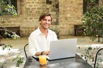 man with a beautiful smile working on a laptop in a street cafe and a place for advertising text...