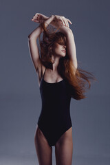 slender woman in black bodysuit posing with raised arms, flowing red hair, neutral gray background,...