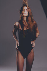 young woman in black bodysuit with long flowing hair stands confidently against gray backdrop with...
