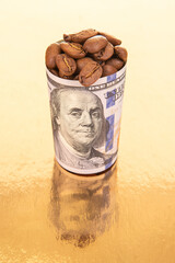On a reflective gold surface, a rolled dollar bill filled with coffee beans stands beside scattered...