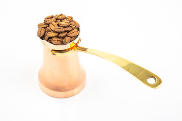 Handcrafted copper cezve with a long brass handle paired with roasted coffee beans on a white...