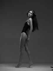 black and white woman in bodysuit posing gracefully with long hair, elegant posture, minimalistic studio background and soft lighting for artistic expression