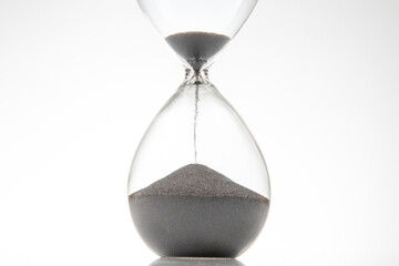 Minimalist hourglass with black sand trickling down on a white backdrop, perfect for concepts of...