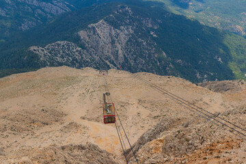 A bright red cable car cabin against the backdrop of lifeless desert rocks.Cabin of cable car on ropeway rises to a top of Tahtali mountain in Kemer, Antalya province, Turkey