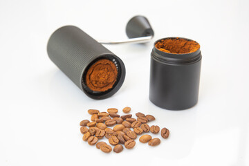 A black manual coffee grinder, disassembled, reveals freshly ground coffee inside, with fine coffee powder spilling out onto a white background for a clean, minimalist look.