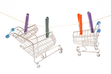 Miniature shopping carts hang on a clothesline with colorful clothespins against a white...