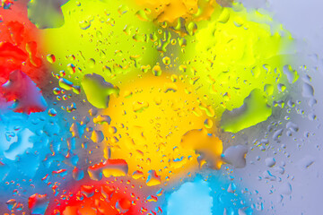 Multicolored water droplets in red, yellow, blue, and green on a reflective surface, ideal for...