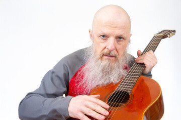 Elderly bald man with a long gray beard performs on a wooden guitar, dressed in a red and gray...