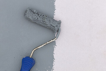Paint roller with blue handle applying gray paint on white wall, concept of renovation and home...