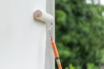 Painting an exterior wall with a white paint roller brush, outdoor home renovation concept.