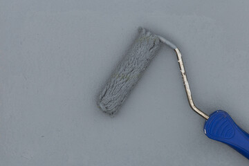 Paint roller with blue handle applying gray paint on wall, top view of painting tool in use.