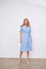 Blonde model poses elegantly in a stylish blue dress in a modern studio setting