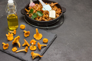 Raw chanterelle mushrooms, onions and oil in bottle on black tray.