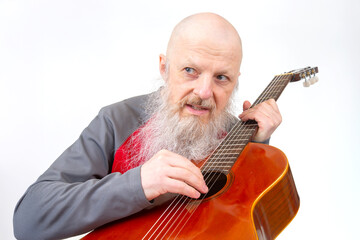 Elderly bald man with a long gray beard performs on a wooden guitar, dressed in a red and gray...