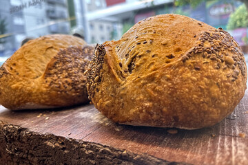 Close-up of two freshly baked, glossy breads topped with seeds, resting on a rustic wooden surface...